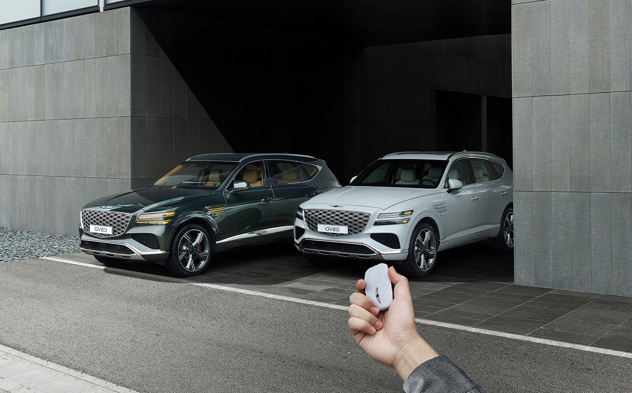 A Vik Black GV80 Coupe and a Uyuni White GV80 Coupe are parked, and the driver is operating the smart key outside the vehicle.