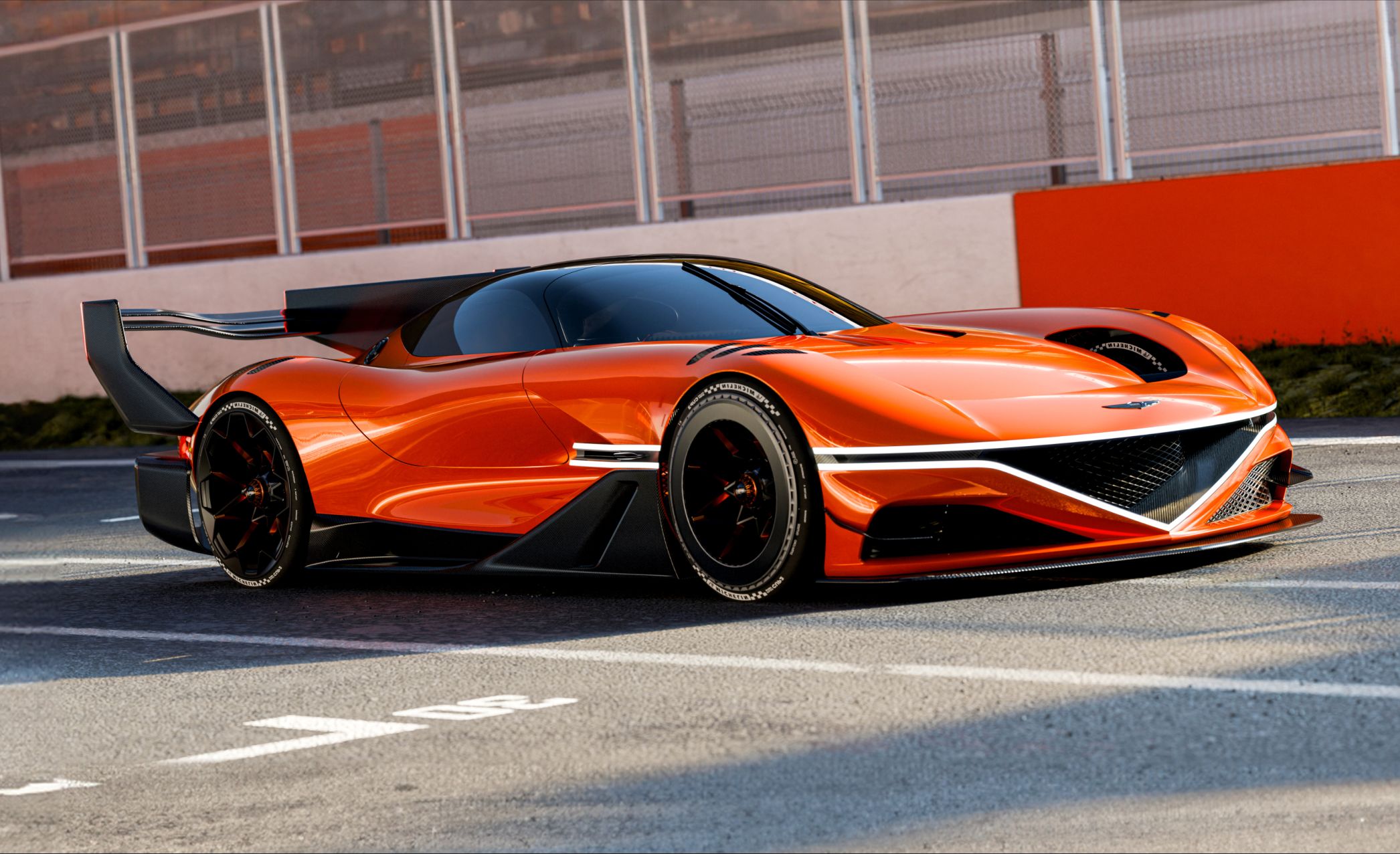 On a clear day at the circuit, the X Gran Racer Concept is parked, showcasing its left side and rear. The prominent rear wing stands out, with the sleek, glossy body reflecting the surrounding scenery. 