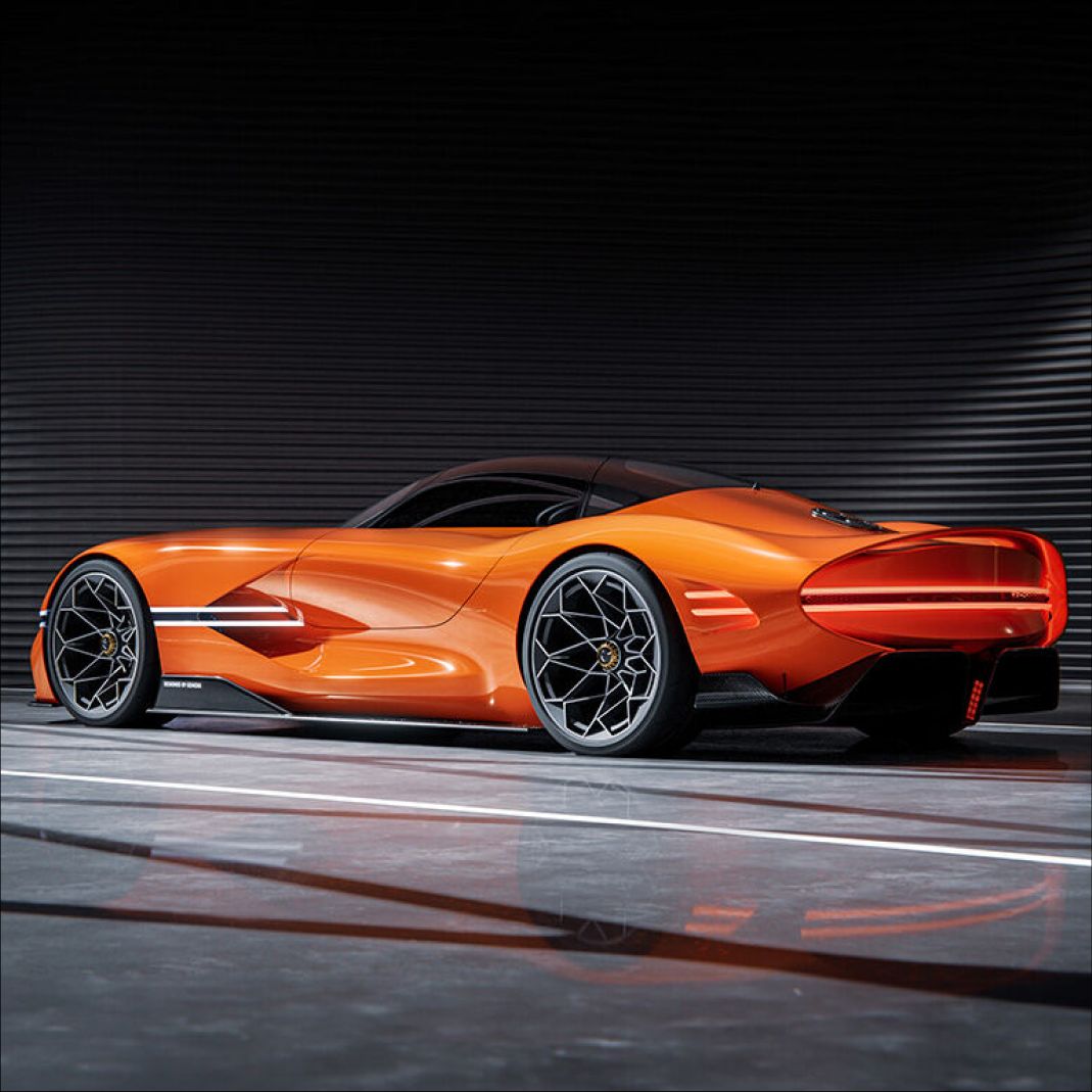 In a dimly lit indoor space, the X Gran Berlinetta Concept is parked, showcasing its side profile. Both the front and rear lights are illuminated, highlighting the prominent fenders arching over the rear wheels. The geometric wheel design stands out boldly at the center of the wheels.