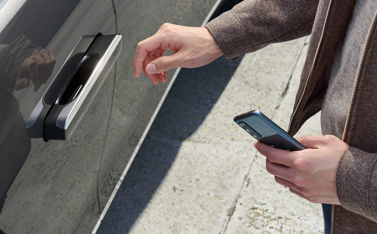 A hand holds a smartphone close to the protuding handle on the door.