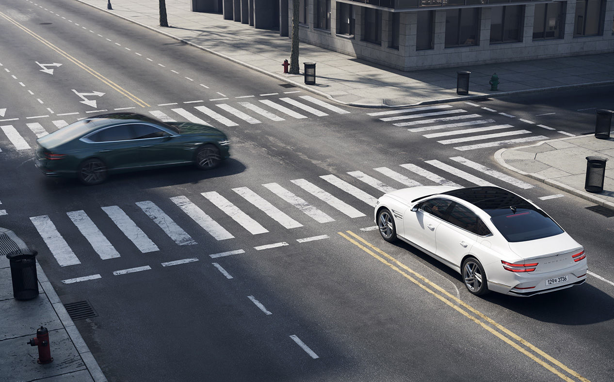 G80 stopped at a four-way intersection with a vehicle passing in front from the left.