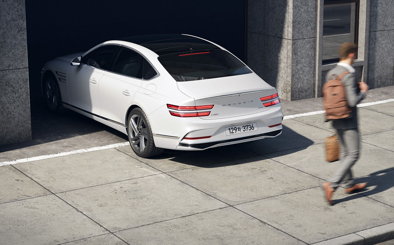 A man passes behind a G80 car that is reversing.