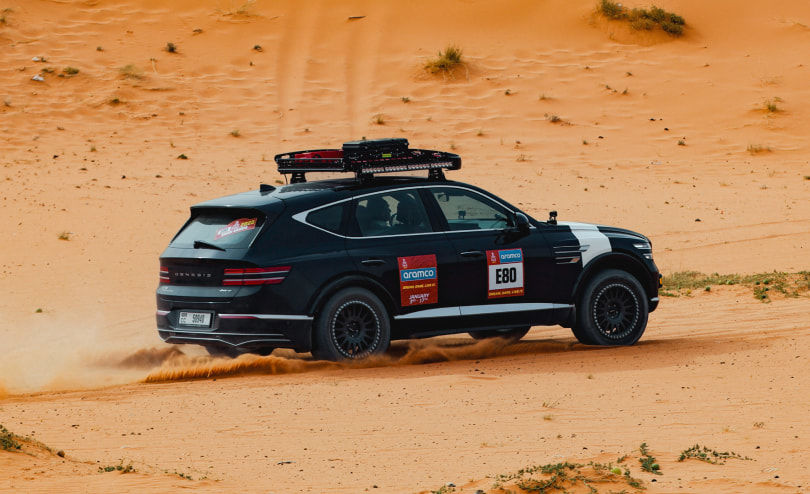 Under the sand dunes, the Genesis GV80 Desert Edition Concept car is driving with a rear view.