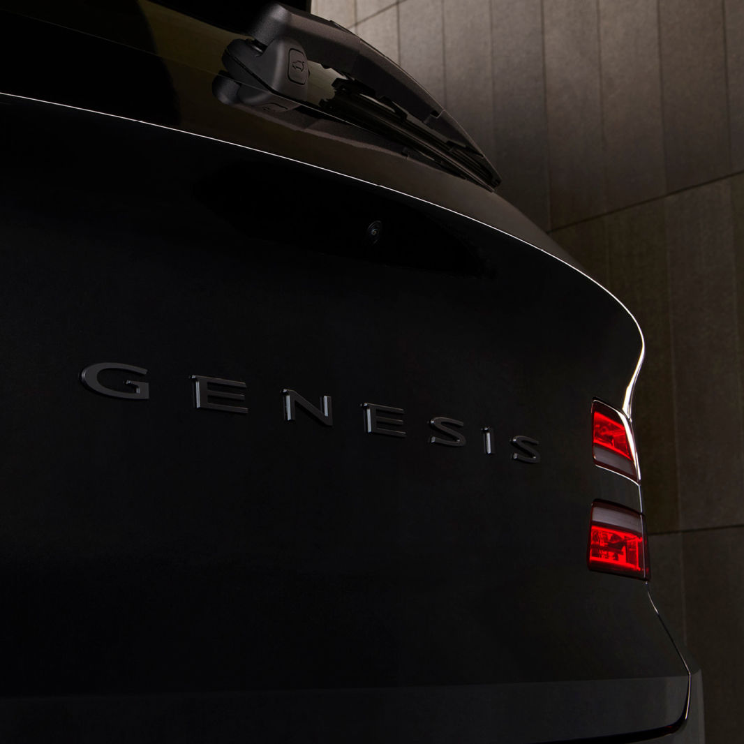 At the rear of the GV80 Black, the metallic lettering that spells 'GENESIS' is visible. Two red light strips are illuminated.
