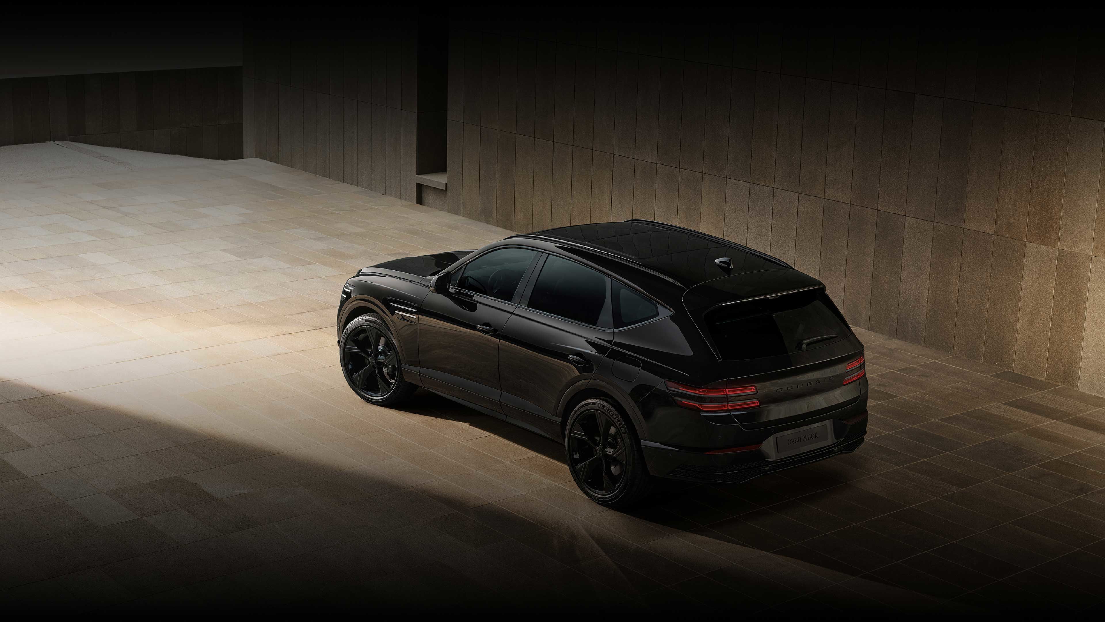 The GV80 Black is seen from the rear side, parked on a tiled floor in front of a gray building.