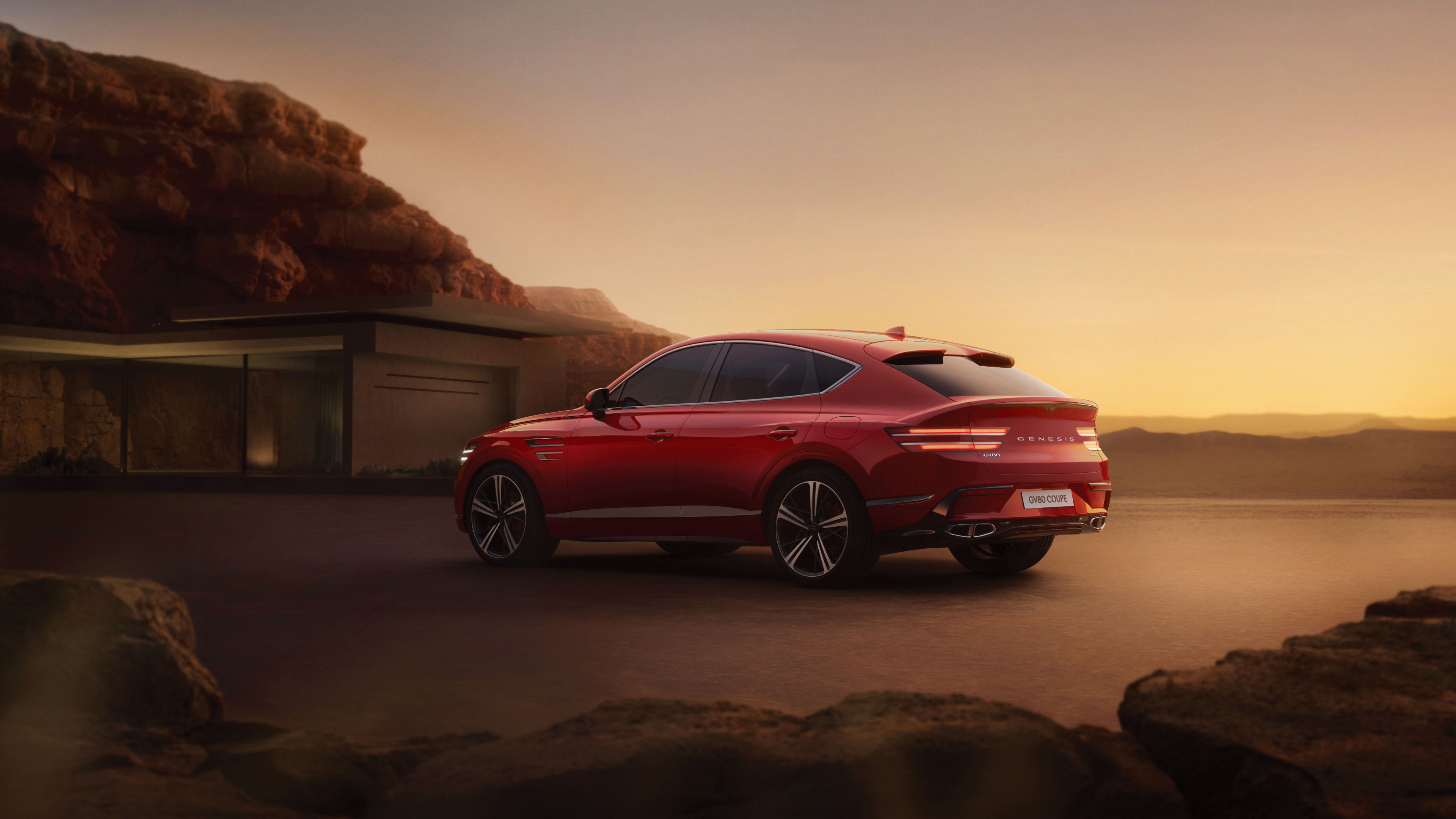 A vibrant red GV80 Coupe is parked, showcasing its rear side in front of a modern building, set against a desert bathed in a soft yellow hue.
